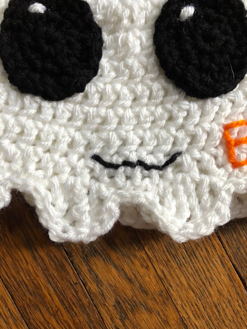 May include: White crocheted ghost hat with black eyes and a stitched-on black mouth. The hat has a scalloped edge.