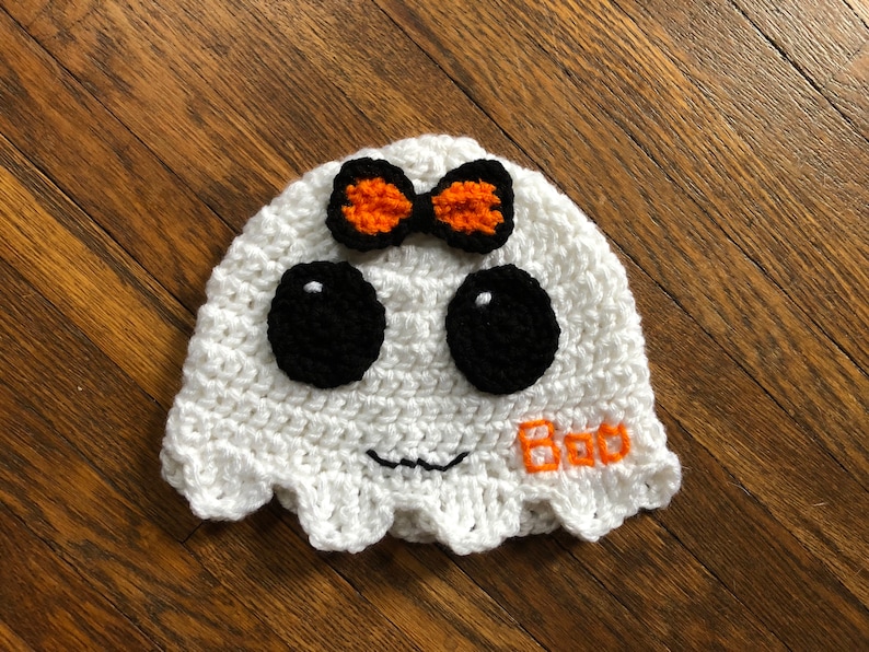 May include: White crocheted ghost hat with black eyes, an orange bow, and the word "Boo" embroidered in orange.