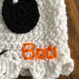 May include: White crocheted ghost hat with a black eye and orange embroidered text that says "BOO".