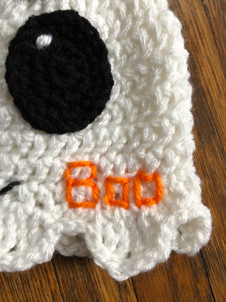 May include: White crocheted ghost hat with a black eye and orange embroidered text that says "BOO".