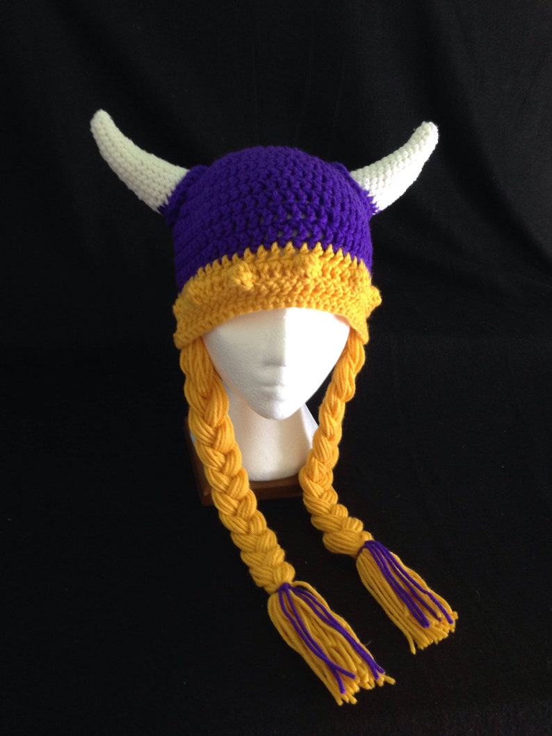 Pu&ograve; includere: Cappello all'uncinetto viola e oro con corna bianche e lunghe trecce gialle.