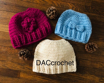 Peut inclure: Trois bonnets en crochet de différentes couleurs : un bonnet rose avec une fleur, un bonnet bleu clair avec un nœud et un bonnet crème. Les bonnets sont sur une surface en bois. DACcrochet
