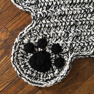 May include: Black and white crocheted rug with a black paw print design.