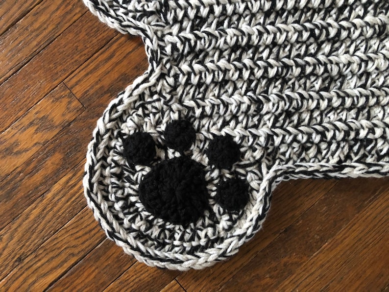 May include: Black and white crocheted rug with a black paw print design.