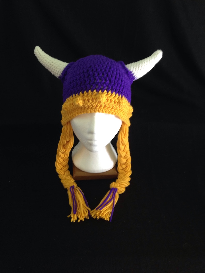 Pu&ograve; includere: Cappello vichingo all'uncinetto viola e oro con corna bianche e lunghe trecce gialle.