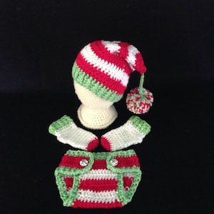 Peut inclure: Une tenue de bébé en crochet rouge, blanc et vert avec un bonnet assorti. Le bonnet a un pompon sur le dessus. La tenue comprend une couche, une paire de chaussons et un bonnet.