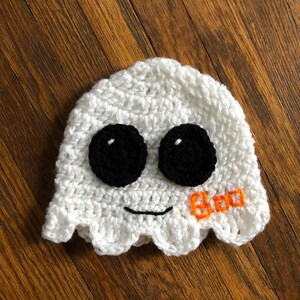 May include: White crocheted ghost hat with black eyes and a stitched orange "BOO" on the side.