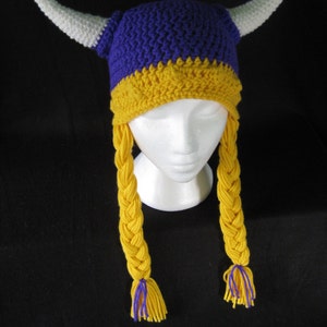 Pu&ograve; includere: Cappello vichingo all'uncinetto viola e giallo con corna bianche e trecce gialle.