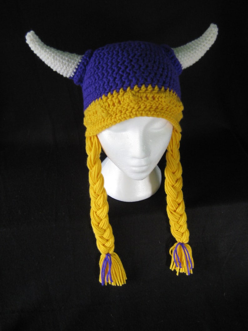 Pu&ograve; includere: Cappello vichingo all'uncinetto viola e giallo con corna bianche e trecce gialle.