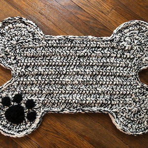 May include: A black and white crocheted dog bone rug with a black paw print in the center.