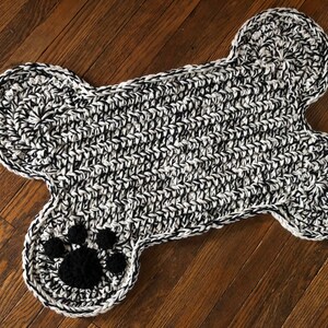 May include: A black and white crocheted dog bone rug with a black paw print in the center.