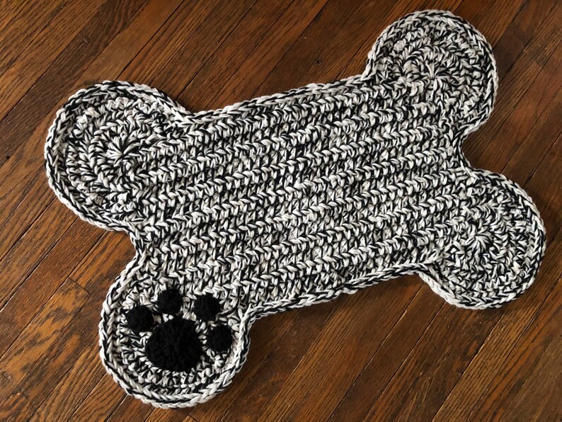 May include: A black and white crocheted dog bone rug with a black paw print in the center.