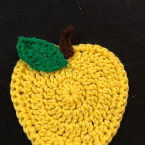 Puede incluir: Una manzana amarilla de crochet con una hoja verde y un tallo marr&oacute;n.