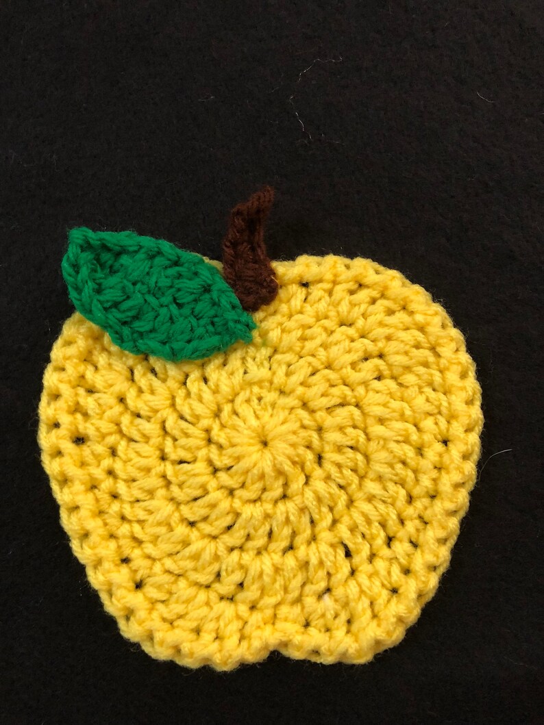 Puede incluir: Una manzana amarilla de crochet con una hoja verde y un tallo marr&oacute;n.