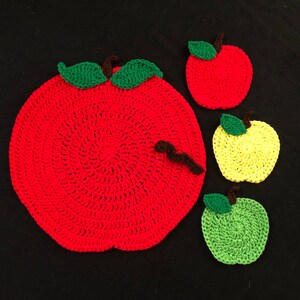 Puede incluir: Conjunto de cuatro posavasos de ganchillo con forma de manzana. Un posavasos grande de manzana roja con hojas verdes y un gusano marr&oacute;n, y tres posavasos m&aacute;s peque&ntilde;os en rojo, amarillo y verde.