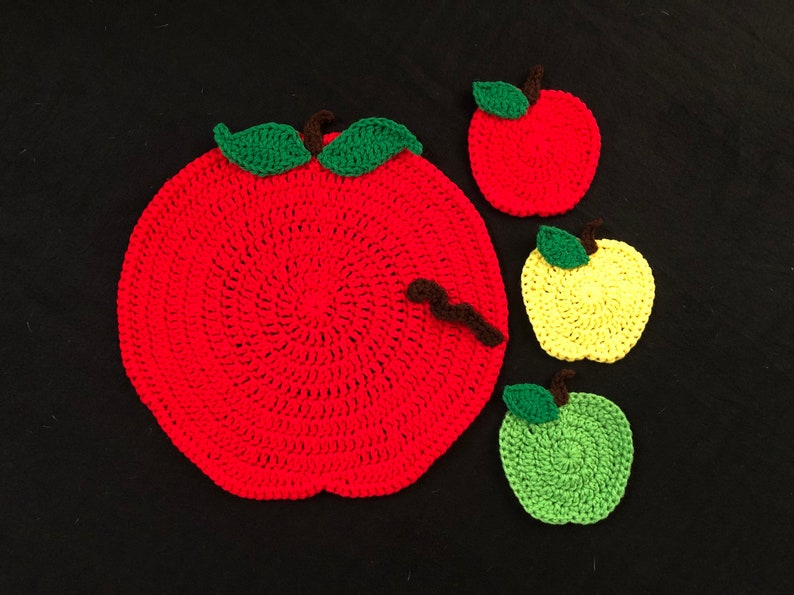 Puede incluir: Conjunto de cuatro posavasos de ganchillo con forma de manzana. Un posavasos grande de manzana roja con hojas verdes y un gusano marr&oacute;n, y tres posavasos m&aacute;s peque&ntilde;os en rojo, amarillo y verde.