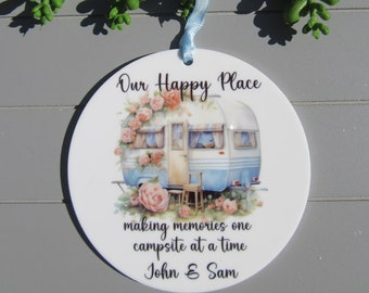 Puede incluir: Adorno de cerámica blanca con una caravana azul y blanca rodeada de flores rosas. El texto dice "Our Happy Place making memories one campsite at a time John & Sam".