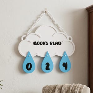 May include: A white cloud-shaped wall hanging with the text BOOKS READ in black. Three light blue teardrop-shaped pendants hang from the cloud, each displaying a black number: 0, 2, and 4. The cloud is suspended by a white plastic chain.