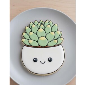 May include: A decorated sugar cookie shaped like a succulent plant in a white pot with a smiling face. The succulent has light green leaves with yellow tips, and the pot has a brown rim and black outline. The cookie is on a gray plate.