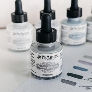 May include: A white ceramic mug with a black handle and the text "But First, Coffee" in a black, handwritten-style font. The mug is on a white surface.