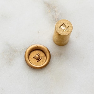 May include: A gold wax seal and stamp featuring a teacup design. The cylindrical stamp and the round seal with the teacup impression are displayed on a white marble surface. Suitable for stationery and craft projects.