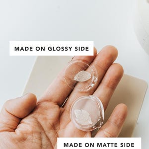 Two clear, wax seals with a leaf design are held in a hand. The text "MADE ON GLOSSY SIDE" and "MADE ON MATTE SIDE" are displayed on the image, indicating the different finishes.