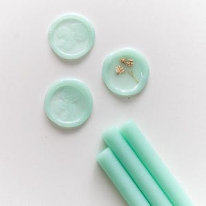 May include: Three teal wax sticks and three teal wax seals, two with a floral design and one with a pressed flower design.