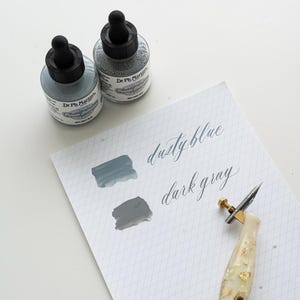 May include: A set of three ceramic mugs with a speckled, matte finish. The mugs are in shades of cream, light gray, and dark gray. Each mug has a simple, minimalist design, perfect for coffee or tea.