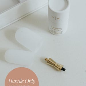 Peut inclure: Un manche de sceau de cire doré avec une vis noire, deux couvercles en silicone blancs et un récipient cylindrique blanc avec l'inscription "Miniature Wax Seal". L'image comprend également le texte "Handle Only" et "Requires Two Wax Seal Heads."