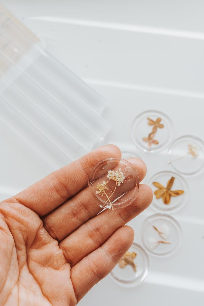 Clear wax seals with dried flowers encased within. One coaster is held in a hand, with others visible. The coasters display different floral designs, offering a natural and botanical theme.