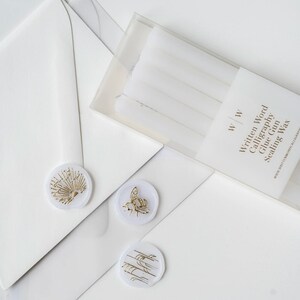 Five vellum wax sticks in a clear plastic box with the text "Written Word Calligraphy Glue Gun Sealing Wax" and the logo "W | W". Three vellum wax seals with gold designs are on a white surface.