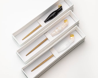 May include: Three calligraphy pens in white boxes. The pens are made of glass and have gold accents. The pens are in different colors: black, white, and clear.
