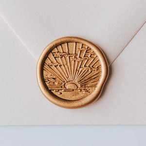 A gold wax seal with a sunburst design. The seal is on a white envelope.