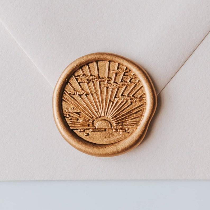 A gold wax seal with a sunburst design. The seal is on a white envelope.