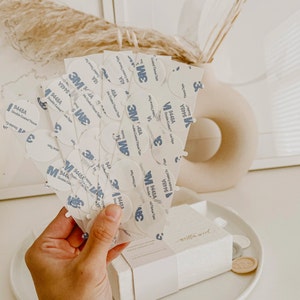 A close-up of a hand holding a stack of 3M brand double-sided adhesive circles.
