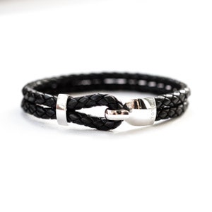 May include: A black leather bracelet with a silver clasp and a silver bead. The clasp has the word "TOTO" engraved on it.