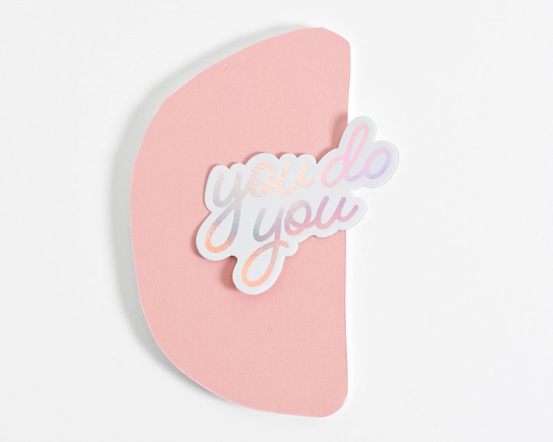 May include: A white sticker with iridescent lettering that reads "you do you" on a pink background.