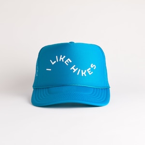 May include: A bright blue trucker hat with a white curved text design that reads "I LIKE HIKES".