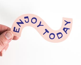 Könnte beinhalten: Ein rosa Papierbanner mit dem Text "ENJOY TODAY" in blauen Buchstaben. Das Banner ist wellenförmig gebogen.