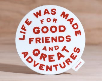 Könnte beinhalten: Ein weißer, runder Aufkleber mit rotem Text. Der Text lautet: "LIFE WAS MADE FOR GOOD FRIENDS AND GREAT ADVENTURES." Auf einer kleinen Lasche steht "peel here."