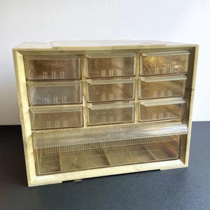 May include: A beige plastic drawer organizer with nine clear drawers and a bottom compartment. The drawers are stacked in three rows of three.