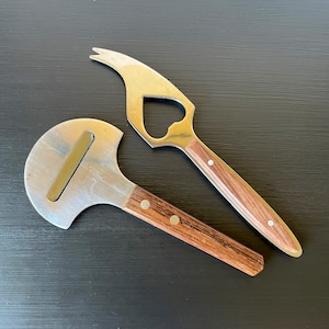 May include: Two kitchen tools with wooden handles. One is a cheese knife with a rounded blade and the other is a bottle opener with a heart-shaped opening.