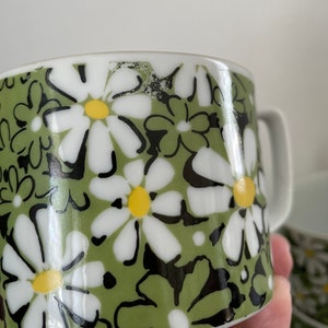 May include: A green ceramic mug with a white daisy pattern. The daisies have black outlines and yellow centers.