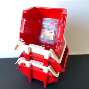 May include: Stackable red and white plastic mini bins. The bins have a rectangular shape with a lip and are designed to stack. The label inside the bin reads "STACKING MINI BIN". The bins are made by Frem Corp.