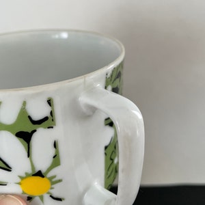 May include: White ceramic coffee mug with a green and black floral pattern. The mug has a white handle.