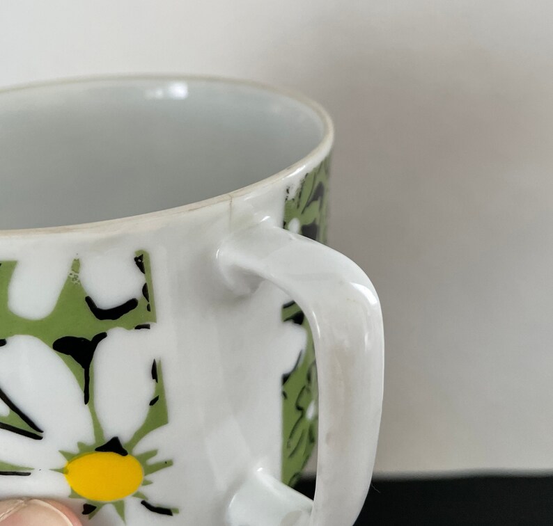 May include: White ceramic coffee mug with a green and black floral pattern. The mug has a white handle.