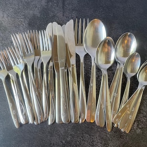 May include: A collection of stainless steel flatware including forks, knives, and spoons. Each piece features a polished finish and a decorative pattern of small, etched starbursts near the base of the handle, creating a uniform set of utensils.