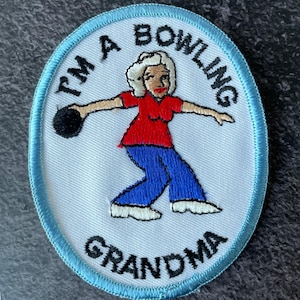 May include: Embroidered patch with a light blue border and the text "I'M A BOWLING GRANDMA". The patch features a cartoon illustration of a woman in a red shirt and blue pants bowling a black ball.