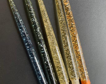May include: Five decorative candles with a glittery finish. The candles are clear with gold and blue glitter. The candles have a brown wooden base.