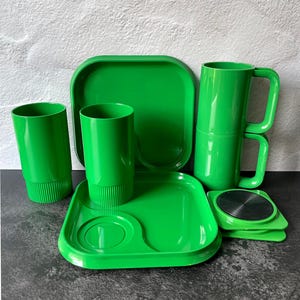 May include: A set of bright green plastic tableware including two square plates with rounded corners, two tall tumblers with ribbed bases, two stackable mugs with square handles, and two small square coasters featuring a black circular center.